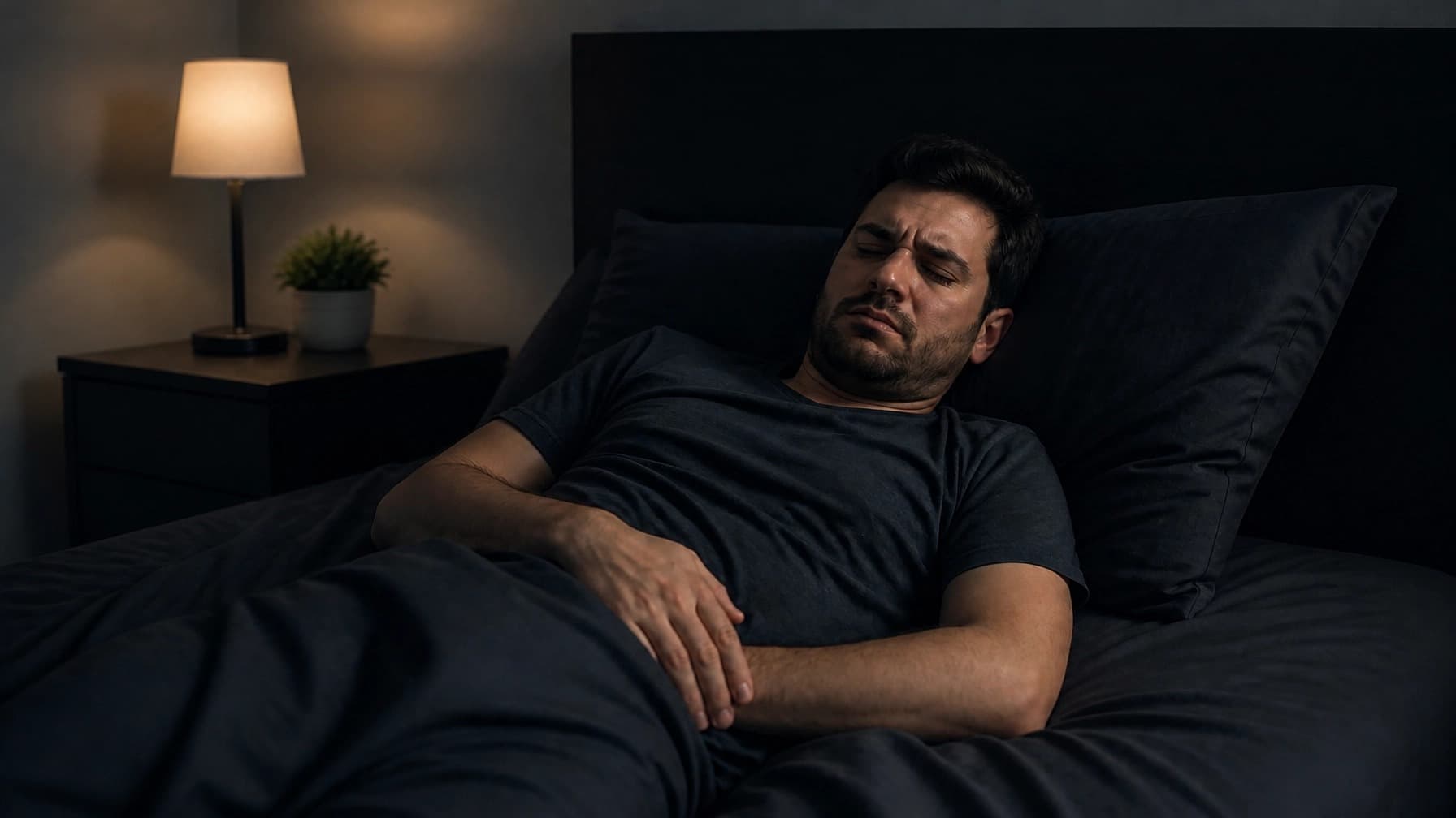 A man lying awake in bed at night, looking uncomfortable.